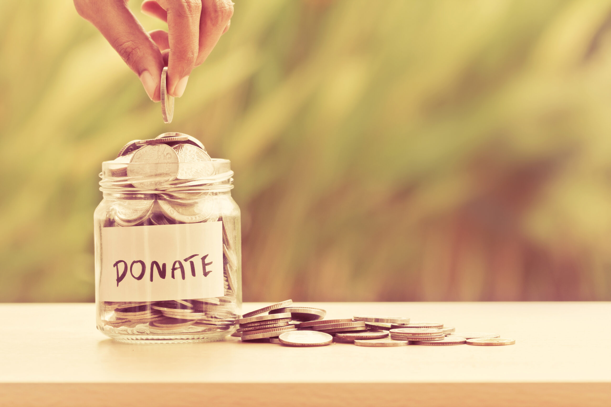 Hand putting coins in a glass jar with donate written on the jar.